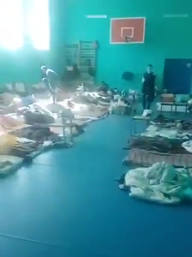 People and bedding on the floor of a sports hall.