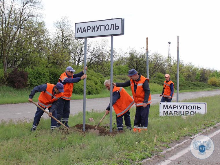 Workers replacing a Ukrainian-language Mariupol road sign with a Russian-language sign.